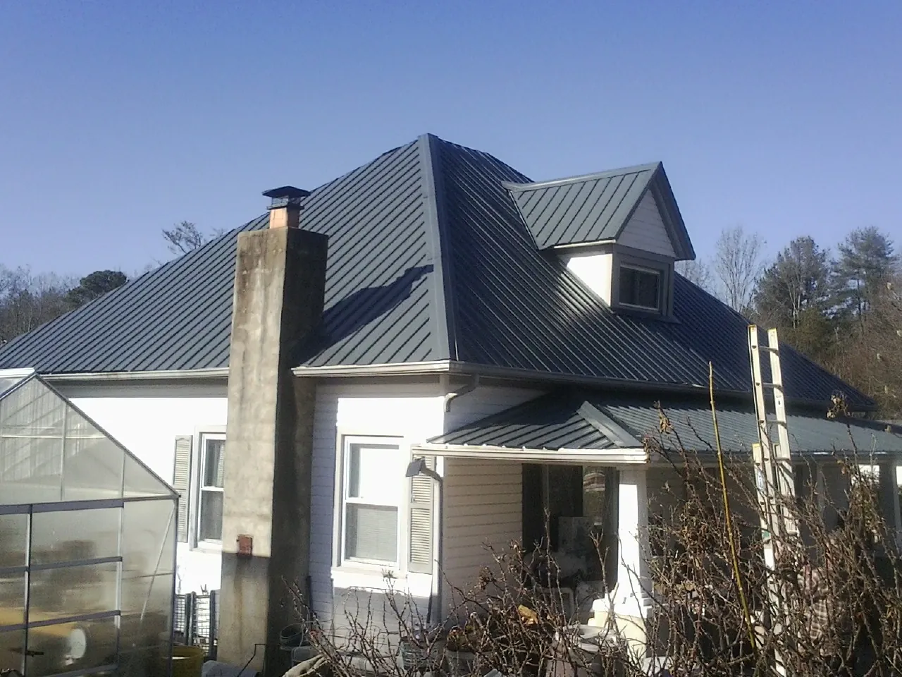 Dark blue standing seam metal roof on a white farmhouse with dormer — Slate & Tile Roof Repair by Roofing Brothers in Grimsley