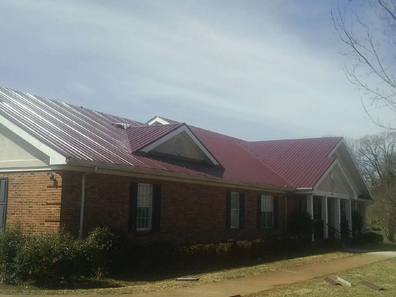 Red metal roof with gabled entries on a long brick building, from a Hail Damage Roof Repair job in Grimsley