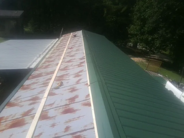 Old rusted panels beside newly installed green metal roofing — Wind Damage Roof Repair by Roofing Brothers in Grimsley
