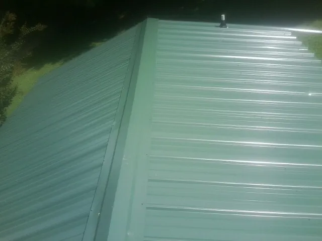 New green metal panels meeting at the ridge of a roof — Flat Roof Repair work by our crew in Grimsley