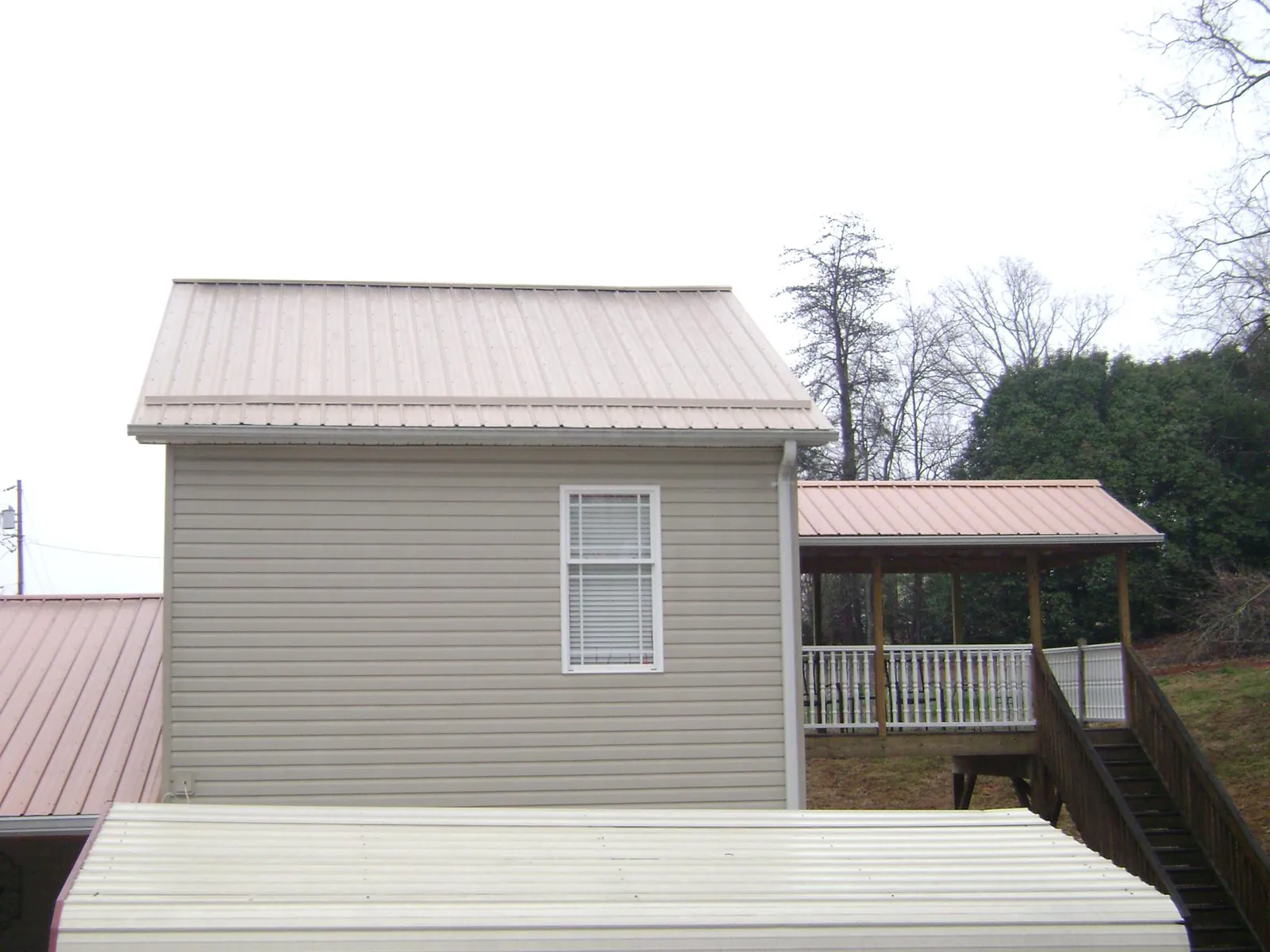 Tan metal roofs on a two story addition and attached porch, from a Roof Replacement job in Grimsley